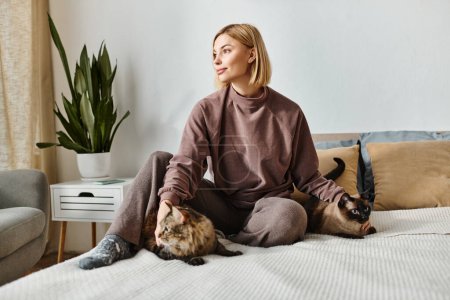 Foto de Un momento sereno capturado como una mujer atractiva con el pelo corto se relaja en una cama con dos gatos mullidos a su lado. - Imagen libre de derechos