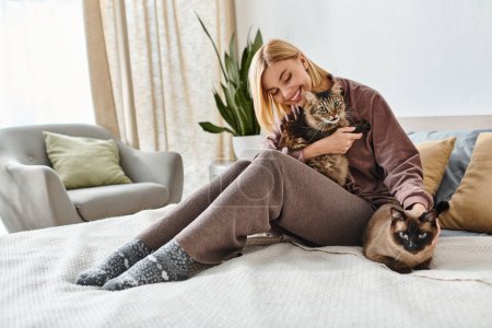 A woman with short hair sitting on a bed, tenderly holding a cat in her arms with a peaceful expression.