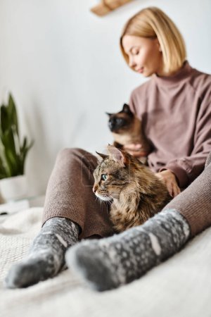 Eine attraktive Frau mit kurzen Haaren sitzt auf einem Bett und hält ihre Katze zärtlich in einem friedlichen Moment zu Hause.