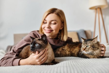 Foto de Una mujer serena con el pelo corto tumbada en una cama rodeada de dos gatos, disfrutando de un tranquilo momento de compañía. - Imagen libre de derechos