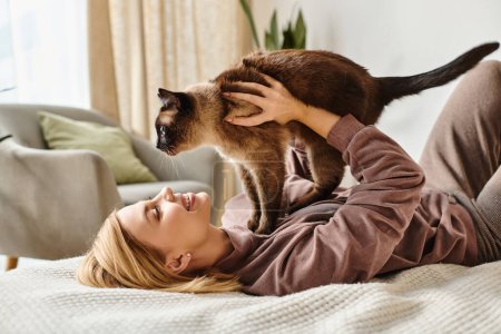 Eine Frau mit kurzen Haaren entspannt auf einem Bett, wiegt ihre Katze in den Armen und strahlt Ruhe und Zufriedenheit aus..