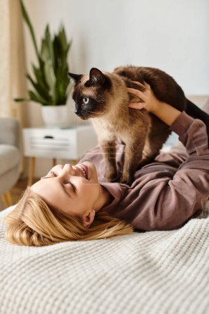 Téléchargez les photos : Une femme aux cheveux courts se relaxant sur un lit, tenant doucement son chat dans un moment paisible à la maison. - en image libre de droit