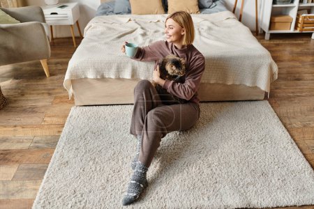 Una mujer serena con el pelo corto se sienta en el suelo, con amor sosteniendo a su gato en un entorno tranquilo en casa.