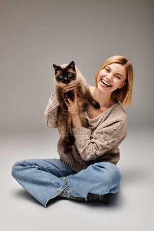 Eine stylische Frau mit kurzen Haaren sitzt auf dem Boden und hält ihre Katze liebevoll in einer warmen Umarmung zu Hause.