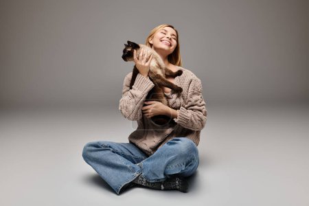 Téléchargez les photos : Une femme aux cheveux courts s'assoit sur le sol, berçant son chat dans un moment de paisible compagnie à la maison. - en image libre de droit