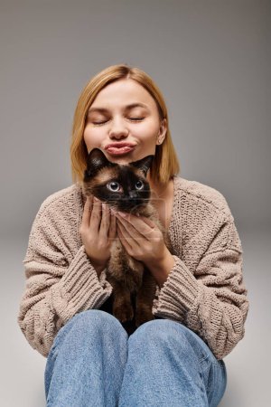 Eine bezaubernde Frau mit kurzen Haaren sitzt auf dem Boden und hält liebevoll eine Katze in einer gemütlichen häuslichen Umgebung.