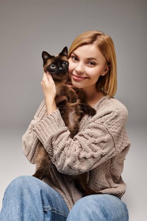 A woman with short hair comfortably sits on the floor, gently holding her cat in a peaceful and loving moment at home.