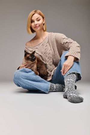 Foto de Una mujer con el pelo corto sentado en el suelo, abrazando amorosamente a su gato mientras comparte un momento de conexión en casa. - Imagen libre de derechos