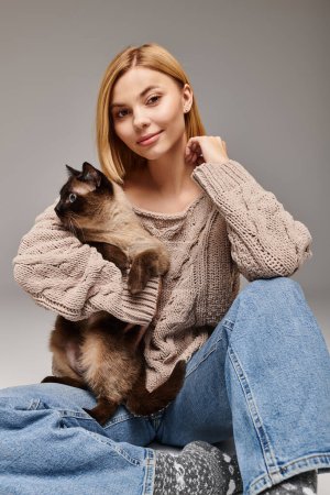 Eine Frau mit kurzen Haaren sitzt auf dem Boden und hält ihre Katze in einem friedlichen Moment zu Hause.