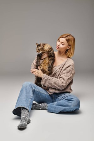 Eine ruhige Frau mit kurzen Haaren sitzt auf dem Boden und umarmt ihre Katze in einem zarten Moment der Geselligkeit und Zuneigung.