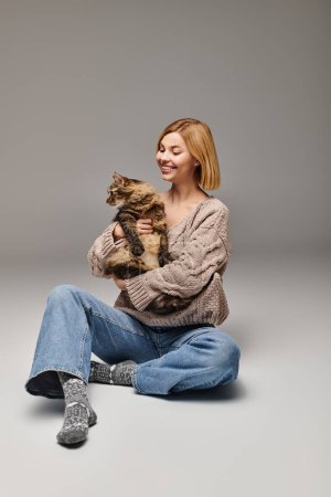 Téléchargez les photos : Une femme aux cheveux courts assise sur le sol, tenant doucement son chat dans un moment paisible et intime à la maison. - en image libre de droit