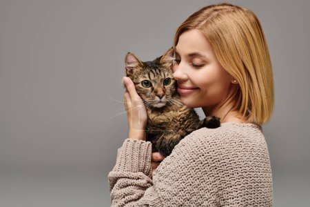 Téléchargez les photos : Une femme aux cheveux courts berçant doucement un chat dans ses mains, montrant de l'amour et des soins dans un cadre confortable à la maison. - en image libre de droit