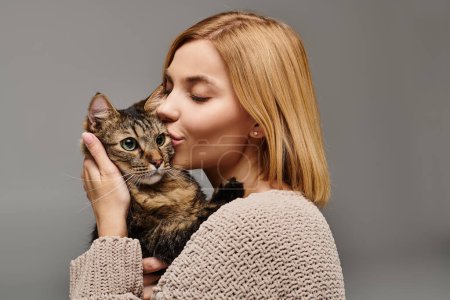 Foto de Una mujer de pelo corto acunando tiernamente a un gato en sus manos, formando un vínculo amoroso entre ellos en casa. - Imagen libre de derechos