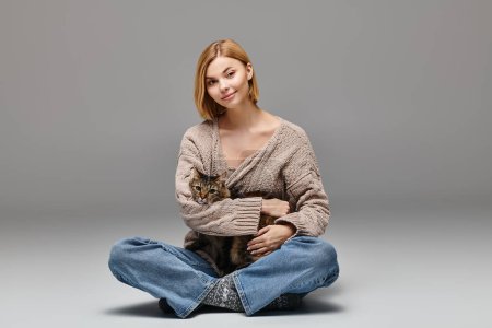 Foto de Una mujer atractiva con el pelo corto se sienta en el suelo, suavemente sosteniendo a un gato en su regazo, disfrutando de un momento tranquilo en casa. - Imagen libre de derechos