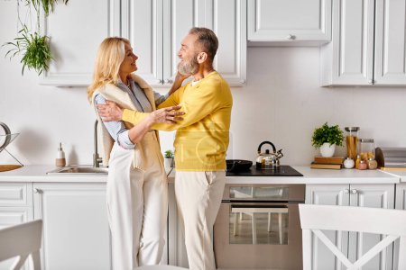 Foto de Maduro hombre y mujer en ropa de casa acogedora, amorosamente pasar tiempo juntos en la cocina en casa. - Imagen libre de derechos