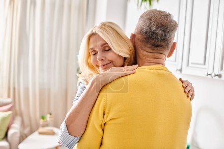 A mature woman in cozy homewear hugs a man in a warm, loving embrace in their living room.