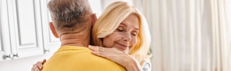Photo for A mature loving couple in cozy homewear, the woman embracing the man in a yellow sweater in a warm, affectionate hug. - Royalty Free Image