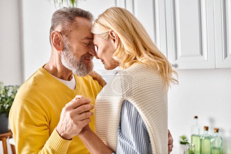 A mature loving couple in cozy homewear embrace in their kitchen, sharing a moment of togetherness.