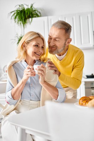 Téléchargez les photos : Un homme et une femme mûrs dans des vêtements confortables assis ensemble à un comptoir de cuisine, profitant d'un moment paisible ensemble. - en image libre de droit