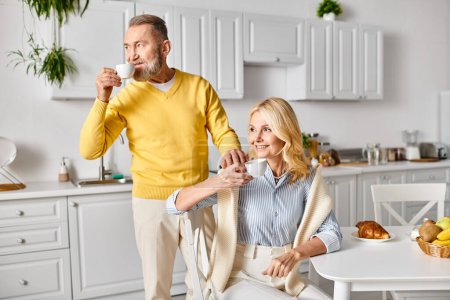 A mature couple in cozy homewear enjoy a moment together at home, sitting at a table and savoring their coffee.