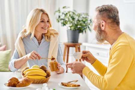 Una pareja madura y cariñosa en una acogedora ropa de casa sentada en una mesa, disfrutando de una comida juntos en una cocina cálida y acogedora.
