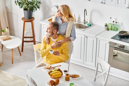 A man and a woman, a mature loving couple, sitting in chairs together, enjoying each others company in cozy homewear at home.