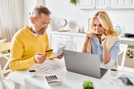 A mature couple in cozy homewear deeply engrossed in reviewing paperwork together at a table in their kitchen.