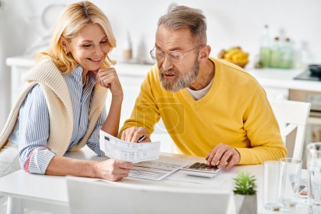 A mature man and woman in cozy homewear are seated in the kitchen, engrossed in reading the newspaper together.