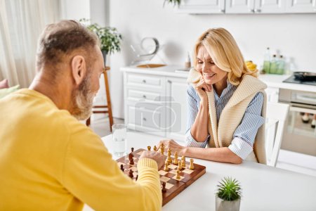 Ein reifes Liebespaar in kuscheliger Hauskleidung, das sich zu Hause auf ein strategisches Schachspiel einlässt.