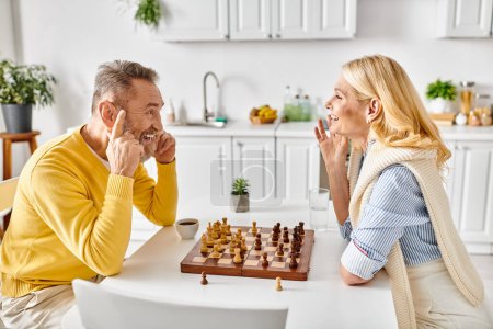Ein Mann und eine Frau in bequemer Hauskleidung sitzen an einem Tisch und spielen Schach, wobei sie sich intensiv auf ihre Züge konzentrieren..
