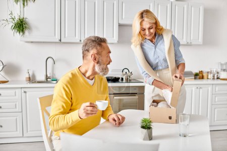 Una pareja madura y cariñosa en una acogedora ropa de casa abre una caja de comida juntos en su cocina en casa.