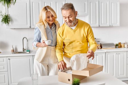 A mature loving couple joyfully opens a box together in their cozy kitchen at home.
