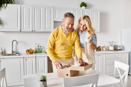 Un homme et une femme mûrs dans des vêtements confortables ouvrent une boîte dans une cuisine confortable, partageant un moment de curiosité et d'anticipation.
