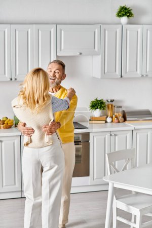 Téléchargez les photos : Un couple aimant mature dans des vêtements confortables danse ensemble dans la cuisine, profitant d'un moment de connexion et de joie. - en image libre de droit