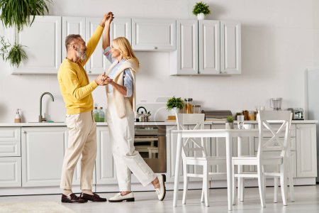 Photo for A mature loving couple in cozy homewear dancing joyfully in their kitchen together at home. - Royalty Free Image