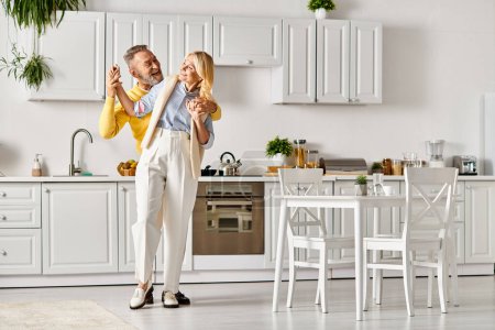 Foto de Una pareja madura y cariñosa de pie en una cocina blanca, vestida con ropa interior acogedora, pasando tiempo de calidad juntos en casa. - Imagen libre de derechos