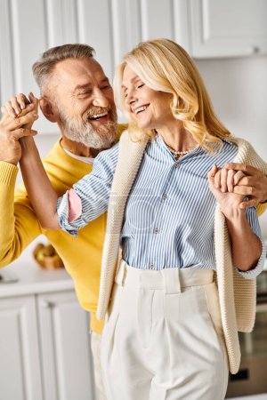 Photo for A mature, loving couple dances in a cozy kitchen, enjoying each others company and the music in their comfortable homewear. - Royalty Free Image