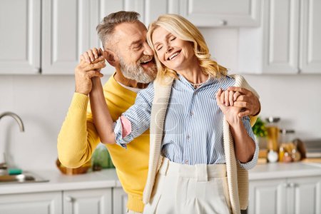 Téléchargez les photos : Un couple aimant mature vêtu de vêtements confortables dansant joyeusement dans leur cuisine à la maison. - en image libre de droit