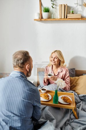 Un couple aimant mature profiter d'un repas confortable ensemble dans leur chambre, assis à une table avec de la nourriture délicieuse.