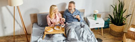 Photo for A mature loving couple, dressed in cozy homewear, sit closely together on a bed, sharing a moment of tenderness and connection. - Royalty Free Image