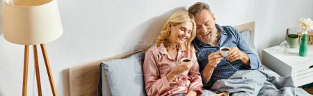 Téléchargez les photos : Un couple aimant mature dans des vêtements confortables, assis sur un lit avec du café - en image libre de droit
