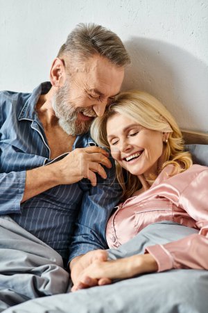 Téléchargez les photos : Un couple aimant mature dans des vêtements confortables couché côte à côte au lit, partageant un moment paisible ensemble. - en image libre de droit