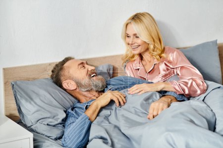 A mature couple in cozy homewear lying together in bed, sharing a quiet and loving moment.