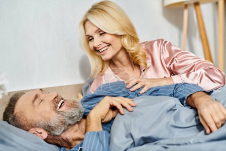 A mature man and woman in cozy homewear lying together on a bed, enjoying a moment of peace and closeness.
