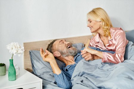 A man and woman, a mature loving couple, in cozy homewear peacefully lay in bed together, sharing a moment of intimacy and closeness.
