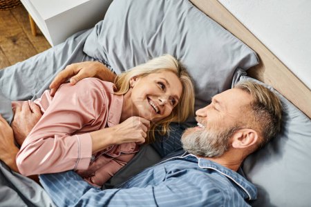 Téléchargez les photos : Un couple aimant mature dans des vêtements confortables couchés ensemble sur un lit, partageant un moment paisible d'intimité et de connexion. - en image libre de droit