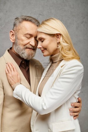 Foto de Debonair pareja con elegante atuendo compartiendo un cálido abrazo contra un sutil fondo gris. - Imagen libre de derechos