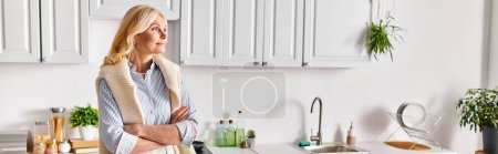 Eine reife, attraktive Frau posiert in ihrem Haus neben einer Küchenspüle und strahlt gelassene Eleganz und Anmut aus.