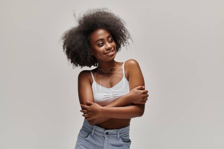 Foto de Una joven afroamericana con estilo se levanta orgullosamente con los brazos cruzados, mostrando su impresionante afro. - Imagen libre de derechos