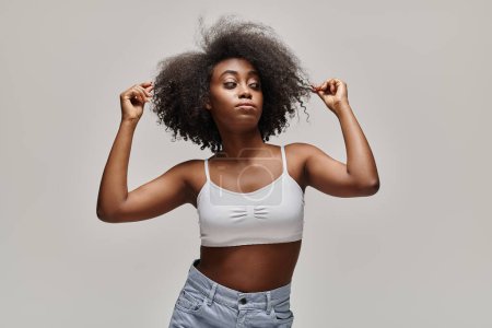 Foto de A beautiful young African American woman with curly hair is striking a pose in a studio setting. - Imagen libre de derechos
